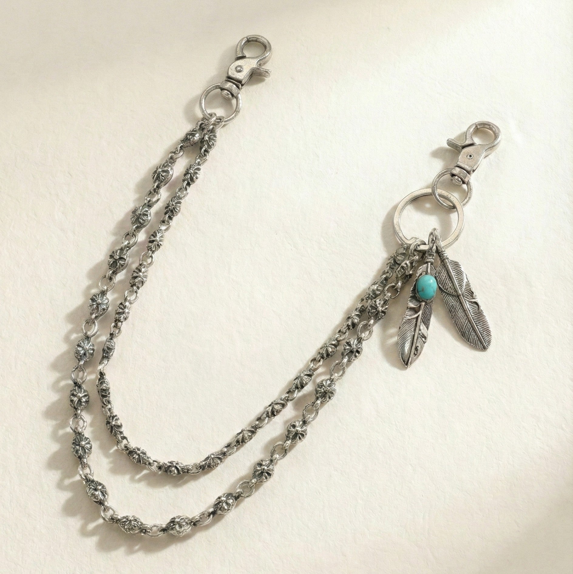 Silver chain bracelet with feather and turquoise charm on a light background